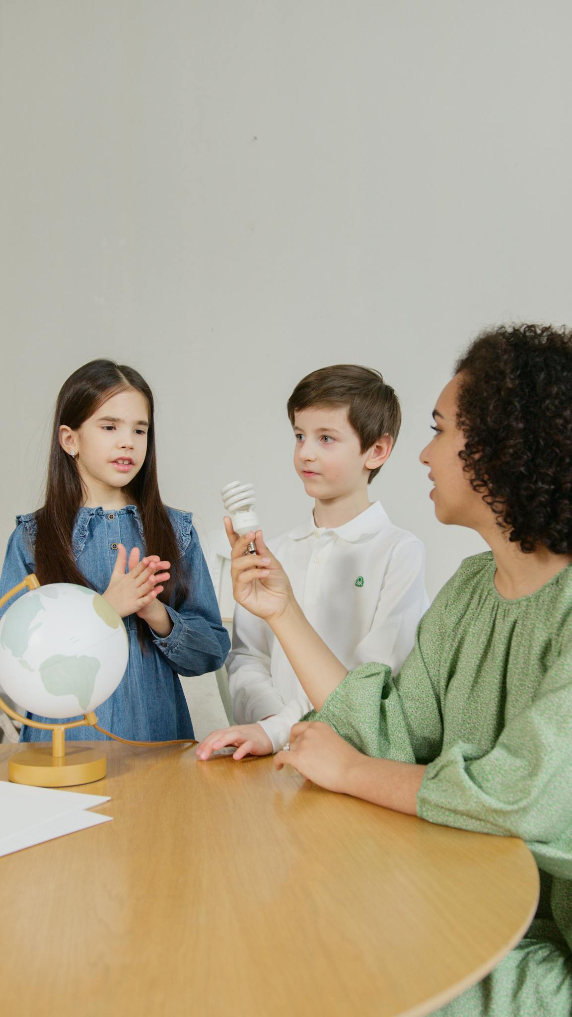 Teacher explains renewable energy concepts to children using a light bulb and globe.